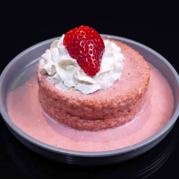Strawberry tres leches cake with whipped cream and a fresh strawberry on top, in a gray bowl.