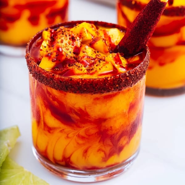 A vibrant mango drink with chili-lime rim, topped with mango chunks and a tamarind candy straw.