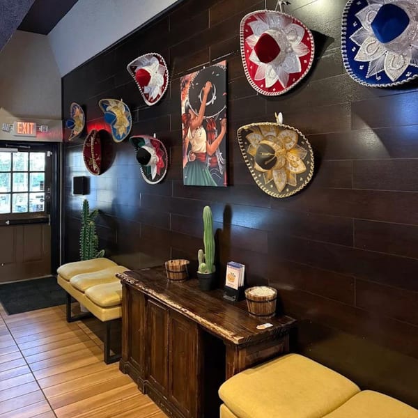 Restaurant entrance with sombreros on a dark wood wall, yellow benches, and a wooden cabinet.