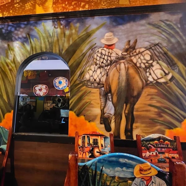A vibrant mural depicts a person leading a donkey laden with baskets, alongside decorative chairs and a mirror.