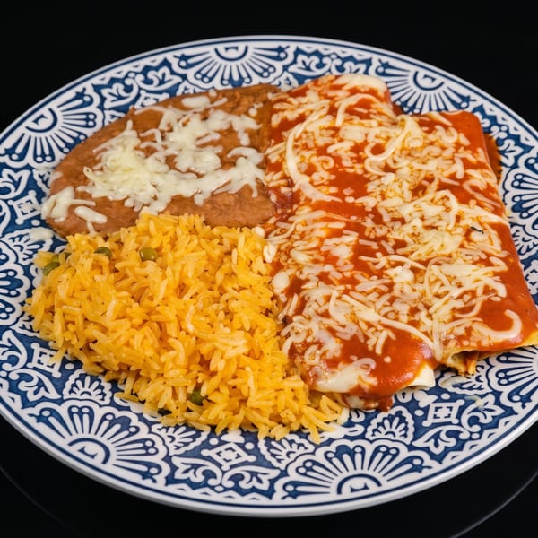 A plate of enchiladas with red sauce and cheese, refried beans, and yellow rice.
