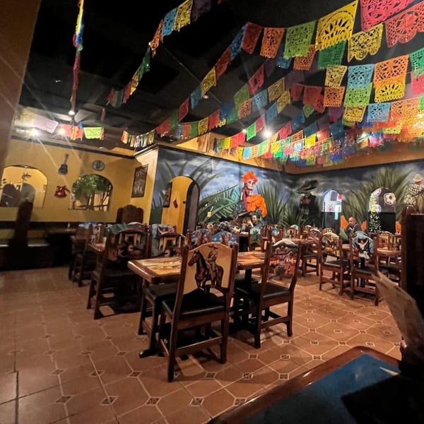 A vibrant Mexican restaurant interior with colorful papel picado banners, murals, and wooden tables and chairs.