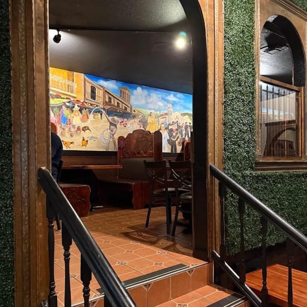 Restaurant entrance with stairs, green wall, and a colorful mural of a town scene.