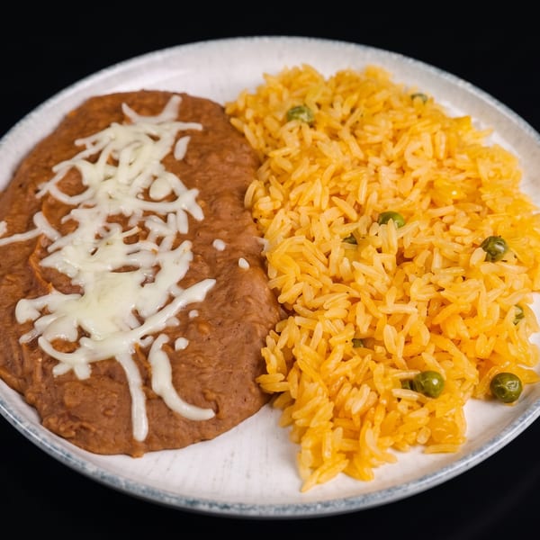 Refried beans topped with melted cheese and yellow rice with green peas on a white plate.