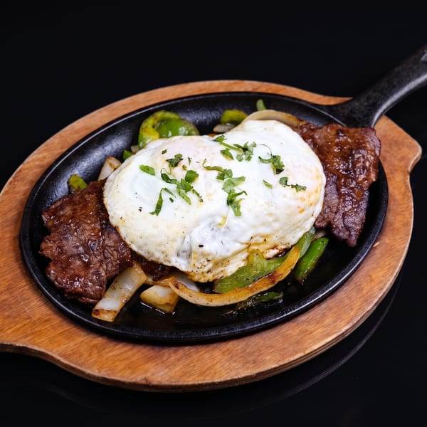 Sizzling steak and vegetables topped with a fried egg and cilantro in a cast iron skillet.