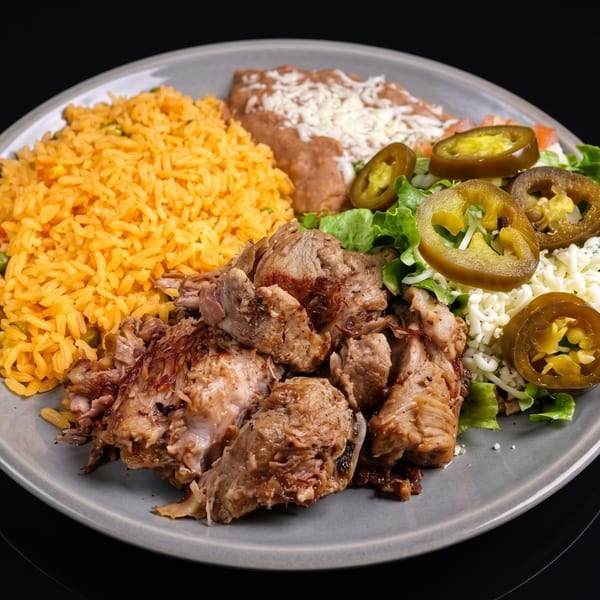 A plate of Mexican carnitas with yellow rice, refried beans, salad, and pickled jalapeños.