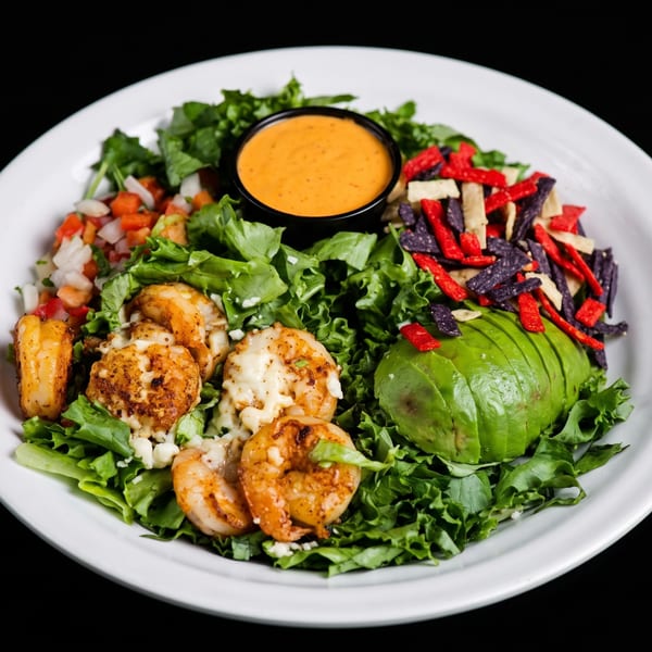 Loaded salad with leafy greens, avocado, grilled chicken, diced vegetables, tortilla strips, and orange dressing.